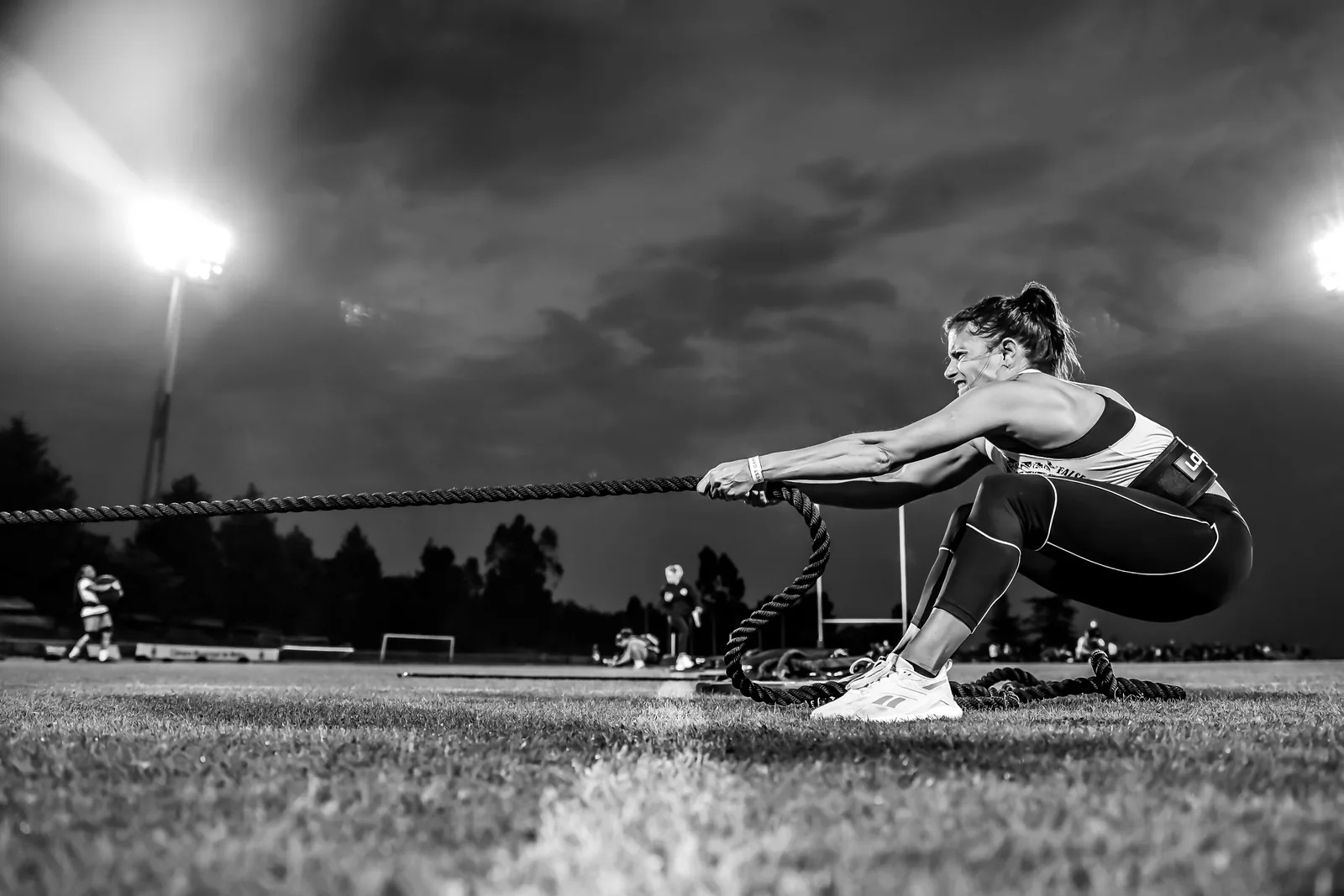 Atleta de crossfit a puxar corda com peso, sob os holofotes do estadio